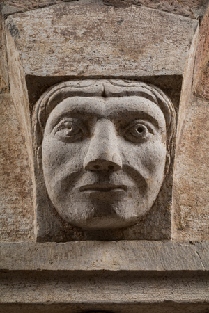 A Corinthian capital with a sculpted face in the abacus protome, by Campionese Masters, XII - XIII century, detail, north wall, Torresani Hall, Ghirlandina Tower, Modena, Italy (photo)