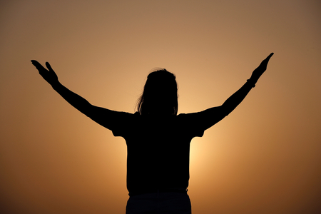 Silhouette at sunset of faithful woman praying. Concept for religion, faith, prayer and spirituality.