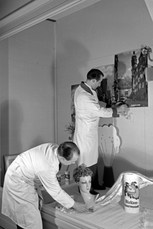Two window dressers preparing a shop window with products produced and sold by the house of beauty, Germany 1930s (b/w photo)