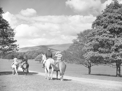 A view of horse riders walking through a piece of open land, fells in the background, 1930s-60s (b/w photo)