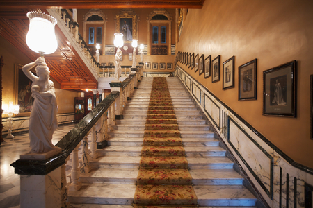 Staircase with photographs lining the wall and statues on the railing in Falaknuma Palace, Hyderabad, Andhra Pradesh, India (photo)
