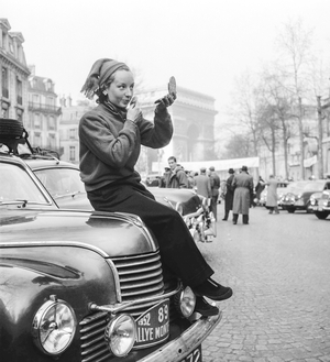 Monte Carlo Rallye, 1952 : a female English competitor making up sitting on her car, Paris, January 24, 1952 (b/w photo)