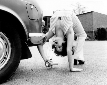 Woman looks under a car with flashlight, England, Great Britain, 1976 (photo)