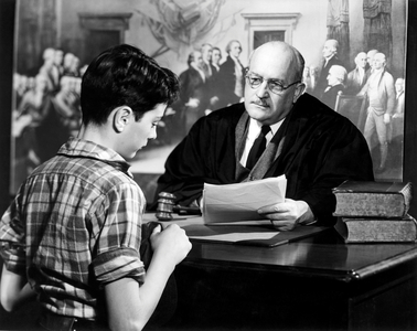 Judge sitting at his desk talking to a boy (b/w photo)