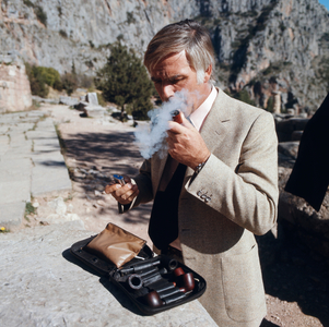 Joachim Fuchsberger pulls on his pipe, which he had previously taken out of his pocket, at the ruins of Delphi, Greece 1970s