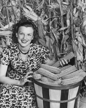 Young woman sitting beside a basket of corn in a corn field