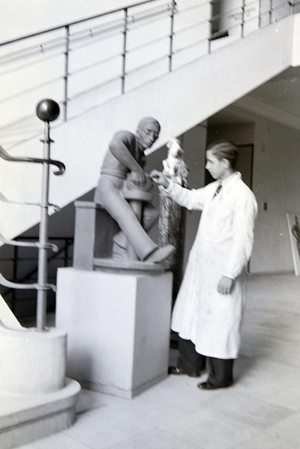 A student of the College for Ceramics in Höhr-Grenzhausen presenting the ceramics exhibited in the hallway of the school, Germany 1930s (b/w photo)