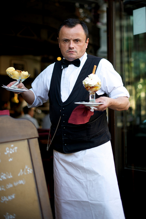A waiter in a Parisian cafe serving ice-cream., 2022 (photo)