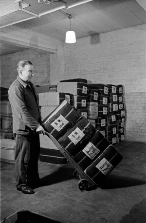 A staff member taking tobbaco bulks at the tobacco silo of the Kyriazi cigarette factory at Hamburg with his barrow, Germany 1930s (b/w photo)