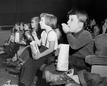 Side profile of a group of children eating popcorn while watching a movie in a movie theater