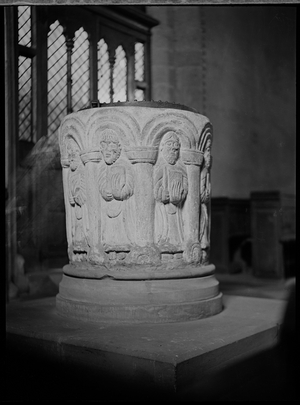 The 12th century font in St George's Church, decoratively carved with a nine bay arcade containing a figure in each bay, 1938 (b/w photo)