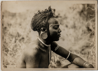 Portrait of a young Masai man, with braided hair collected in a typical hairstyle and the ear lobe deformed by a clay disc, Africa, 1930 (photo)