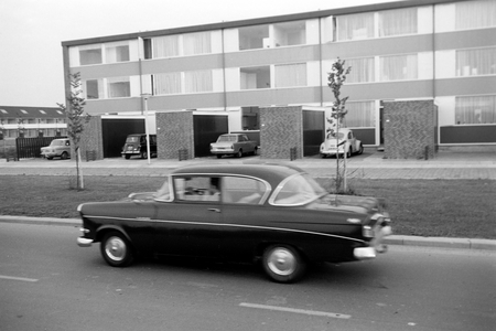 A vintage car driving on a road in front of new housings, Netherlands 1971