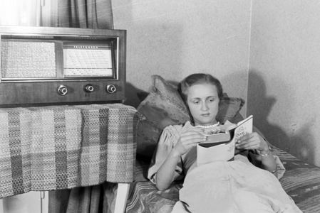 A woman lying on a sofa while listening to the radio, Germany 1930s (b/w photo)