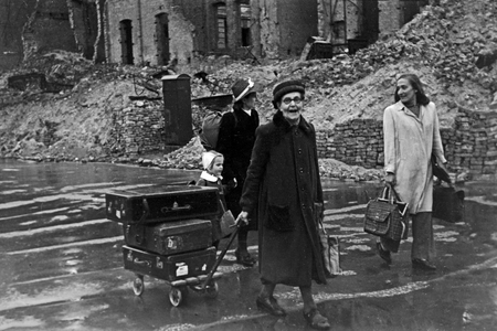 Little girl with her dolls in a backpack and her family on her way throuhgh the rainy Berlin, Germany 1949