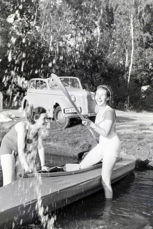 Two young woman are getting inside a boat with a paddle on a lake, Germany 1930s (b/w photo)