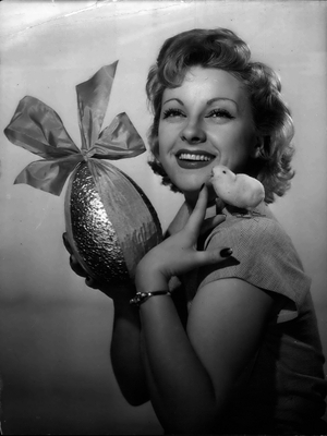 Young smiling woman holding an Easter egg and a little chick, 1953 (b/w photo)