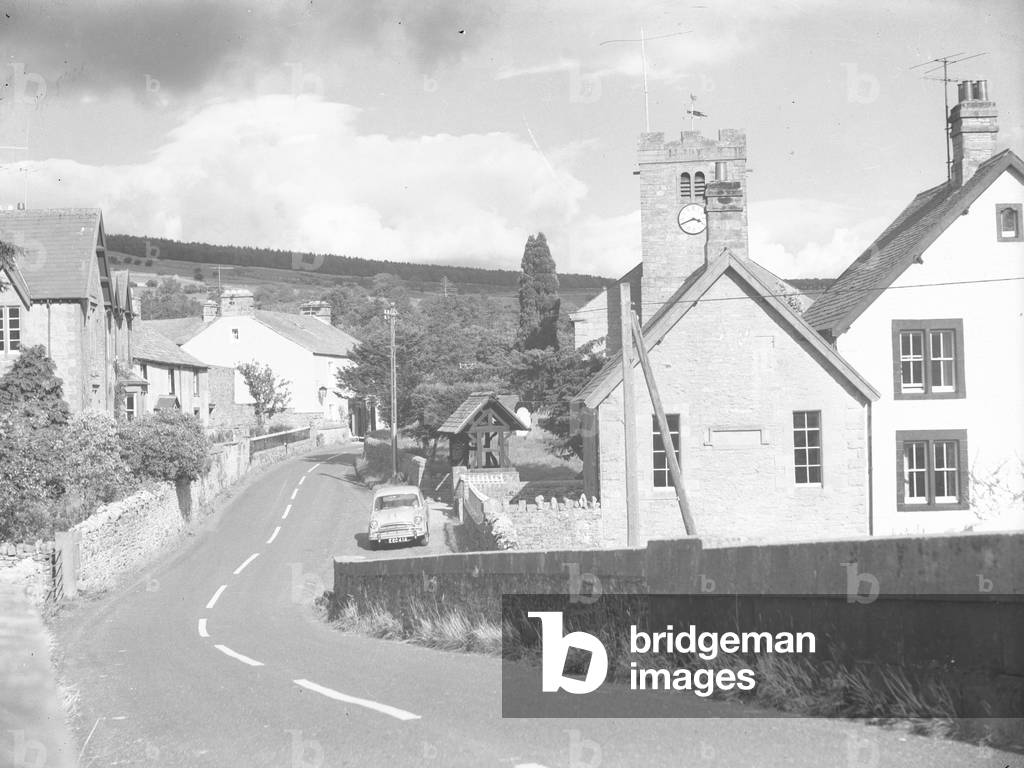A view looking through what appears to be Brampton village, with a road through the centre lined by buildings and a church; architecture; religious; ecclesiastical; on the right, 1930s-60s (b/w photo)