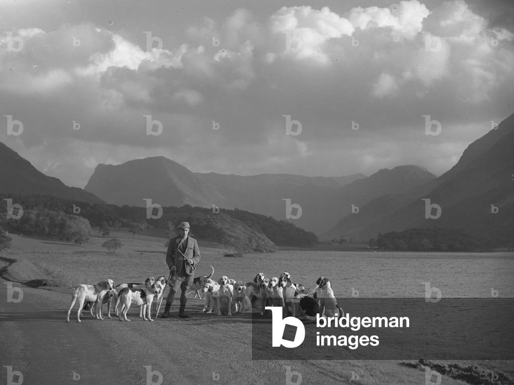 A man stands next to a lake with hounds at his feet, 1930s-60s (b/w photo)
