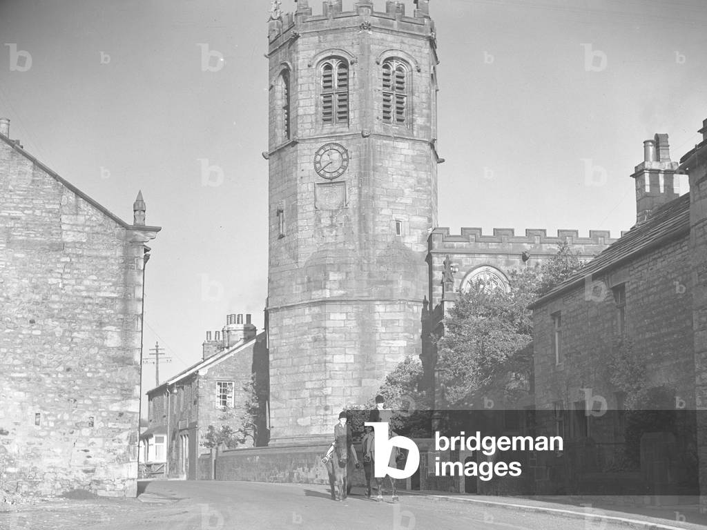 Two young horse riders walking through Horny, St Margarets church; architecture; religious; ecclesiastical; is behind them, 1930s-60s (b/w photo)
