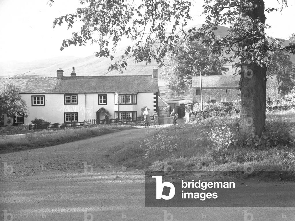 Children cycling down road towards camera at Dufton with buildings in background, 1930s-60s (b/w photo)