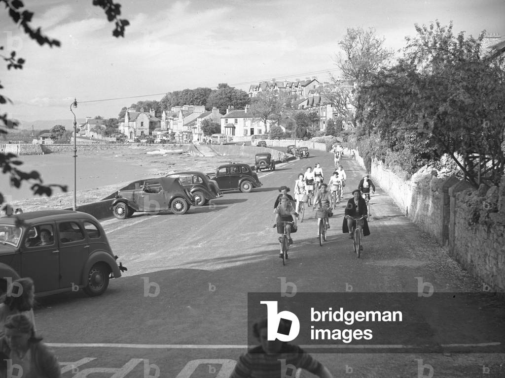 Cyclists on road riding towards camera, 1930s-60s (b/w photo)