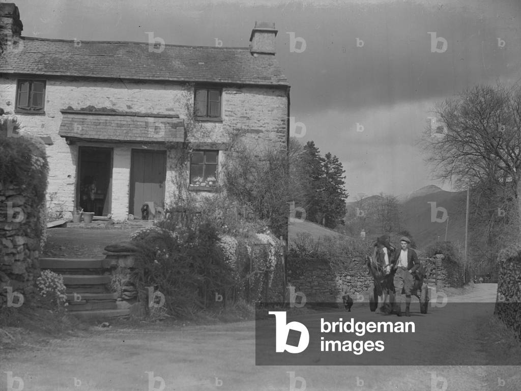 To the right of the image a man leads a horse and cart, to the left of image some cottages, 1930s-60s (b/w photo)