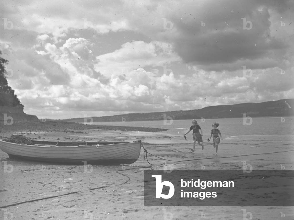 Children running towards beached rowing boat carrying sea; seascape;weed, 1930s-60s (b/w photo)