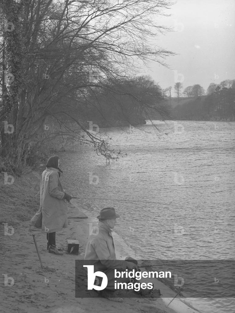 A man and women fishing at the edge of a river, 1930s-60s (b/w photo)
