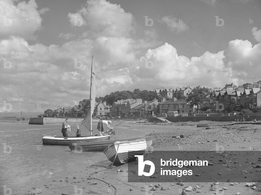 Two sailing dinghys beached on shore with family making one ready, 1930s-60s (b/w photo)