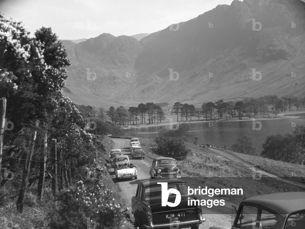 Cars parked along narrow road next to Buttermere including MGB roadster, 1930s-60s (b/w photo)