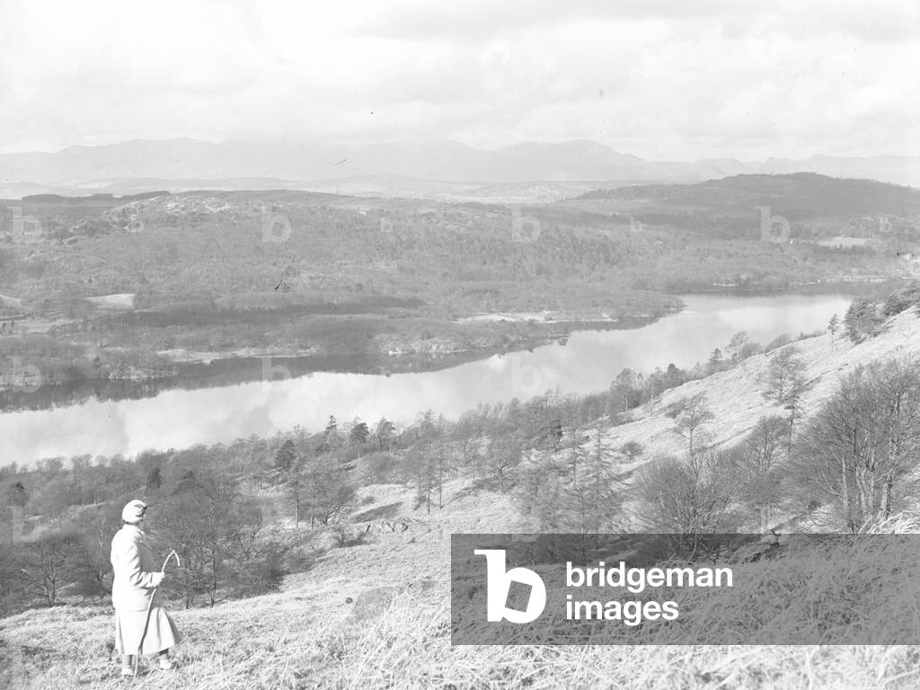 A woman walks in the hills above a lake, fells in background, 1930s-60s (b/w photo)