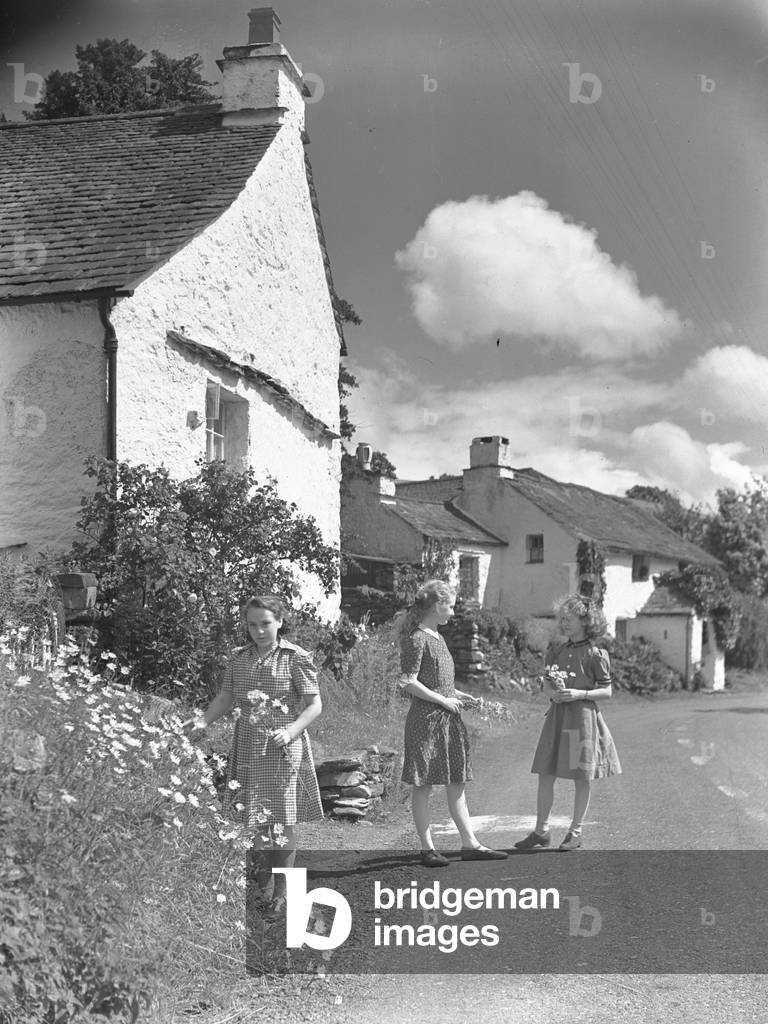 Three girls stood at a road side talking and picking flowers, 1930s-60s (b/w photo)