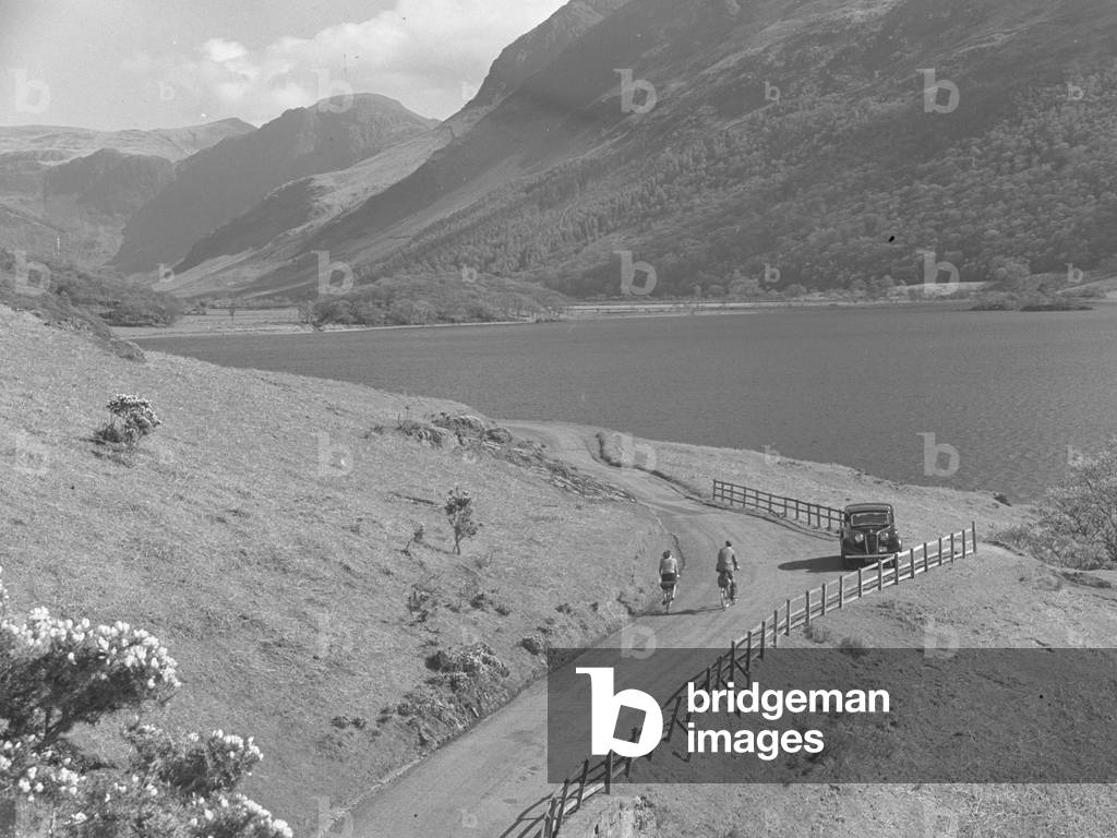 View across a road alongside Crummock Water, the lake and fells in the background, 1930s-60s (b/w photo)