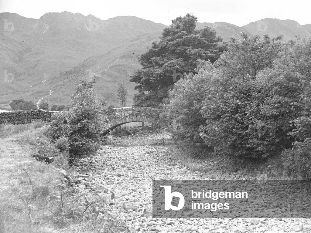 Closeup view of stones in dry river bed with bridge in background, 1930s-60s (b/w photo)