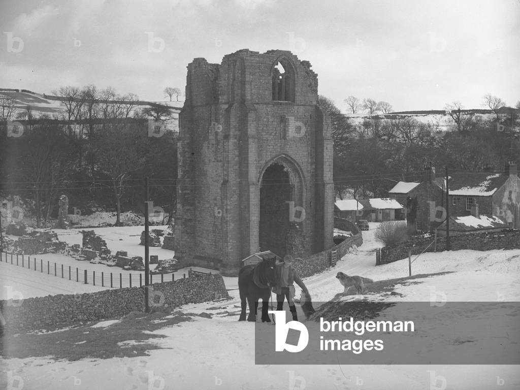 Boy with horse and two dogs in front of Shap Abbey in snow, 1930s-60s (b/w photo)