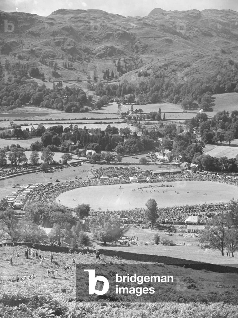 Fell runners coming up hill and looking down on crowds at Grasmere sports, 1930s-60s (b/w photo)
