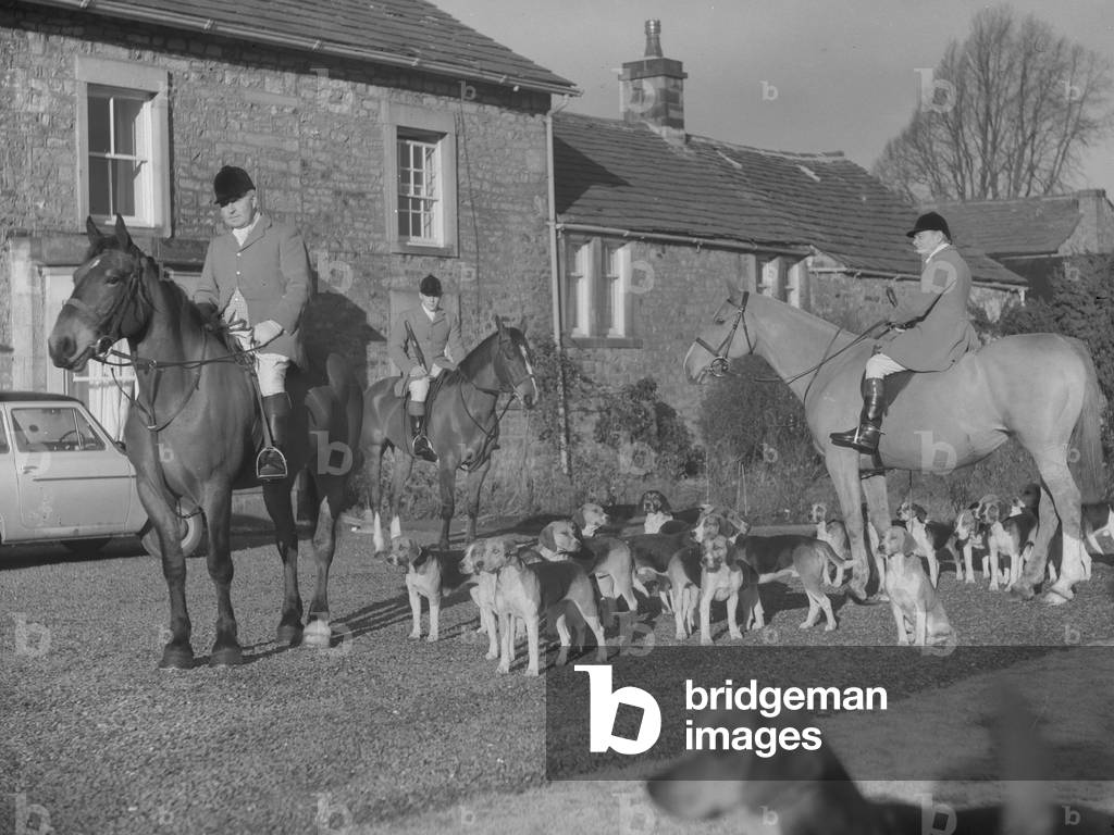 A view of huntsmen on horses and hunting hounds, all standing in front of a building, 1930s-60s (b/w photo)