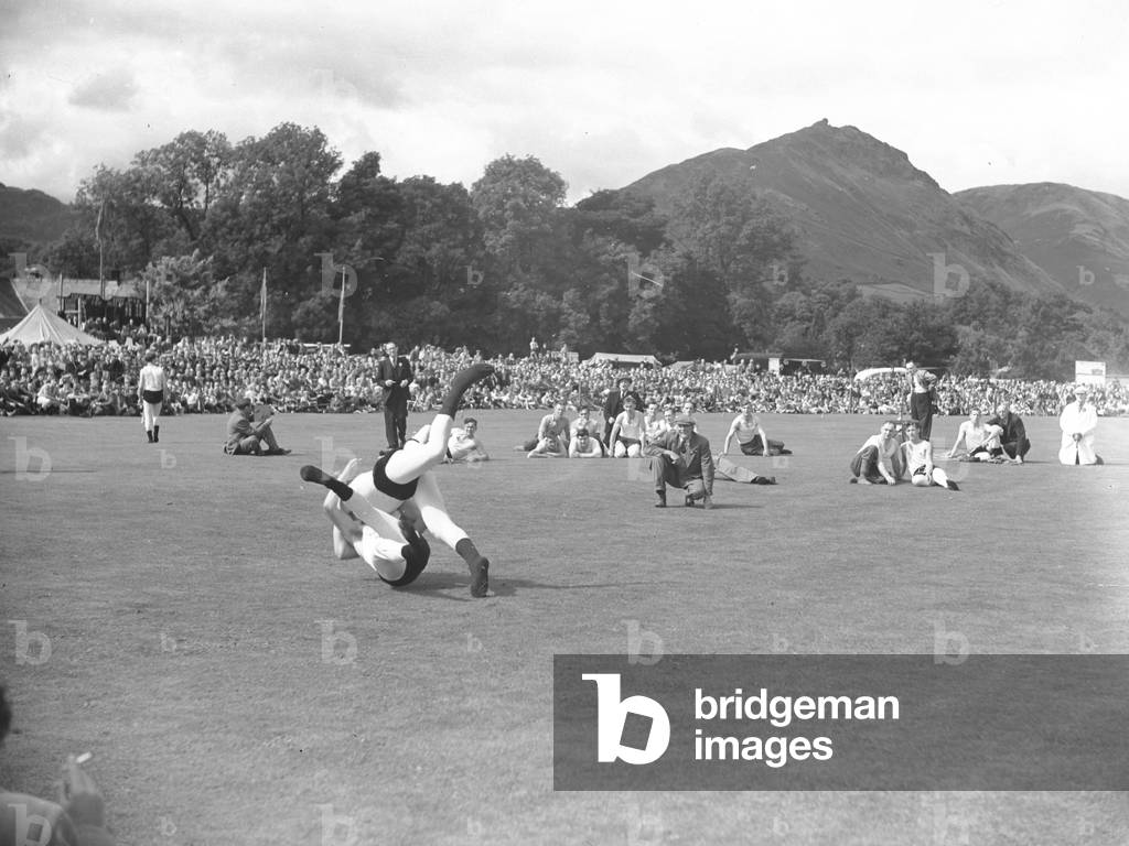 Two wrestlers wrestling with referee and crowds watching, 1930s-60s (b/w photo)