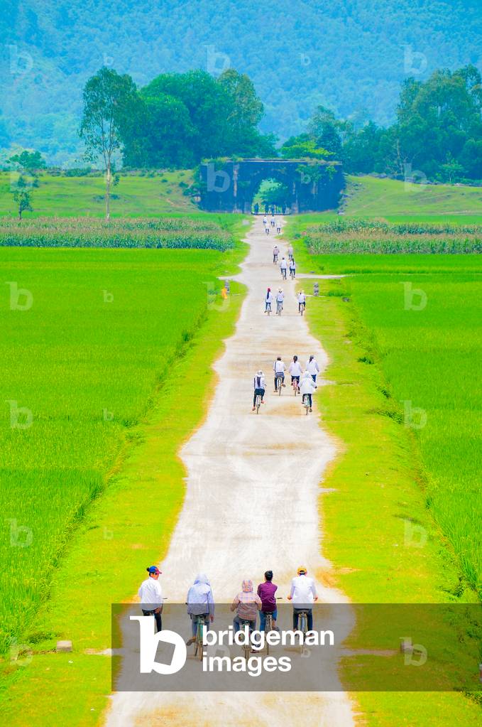 Schoolchildren cycling towards north gate of Ho Citadel, Vietnam (photo)