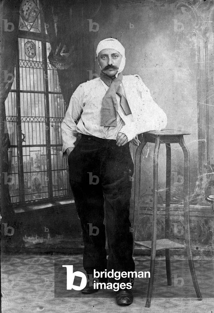 Portrait of a wounded man (Invalid of the First World War 1914-1918). He has a bandage on his head and his arm breaks in the plaster. Postcard