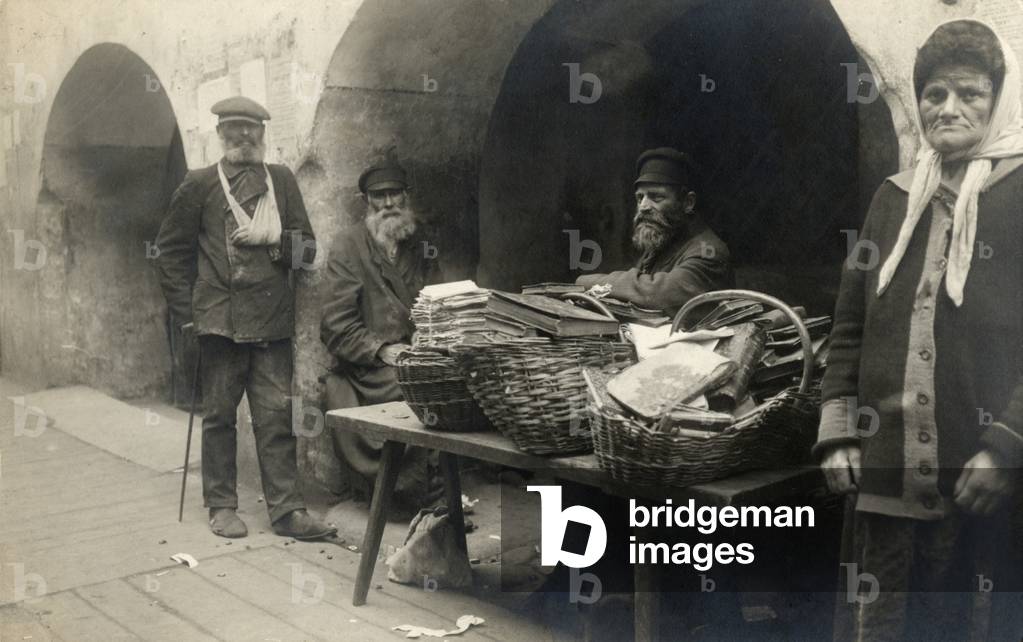 Bookseller selling books in baskets in Vilna, Lithuania, 1914 three men and one woman standing under arches in the street