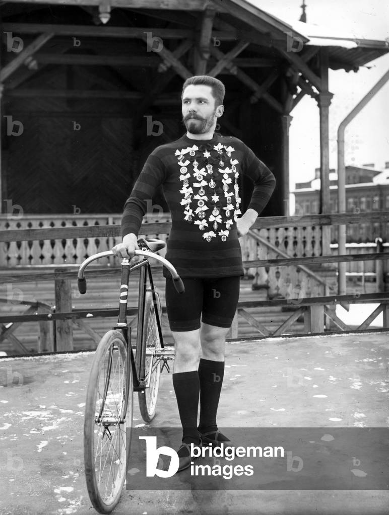 Winner of a cycle race in St. Petersburg displaying his various medals (b/w photo)