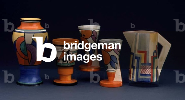 (LtoR) A 'Blue W' pattern Mei Ping vase, a 'Trees and House' pattern vase, a pair of 'Oranges' pattern Yo-Yo vases and a 'Tennis' pattern conical jug by Clarice Cliff (1899-1972) (ceramic)