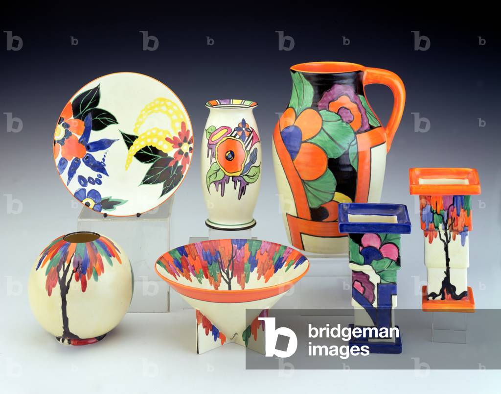 (LtoR) A 'Latona Blossom' plate, a 'Latona Cartoon Flowers' pattern vase, a 'Latona Orange Dahlia' single handled Lotus jug, a 'Latina Tree' pattern Globe shape vase, a 'Latona Tree' pattern conical bowl and two 'Latona Tree' pattern vases, by Clarice Cliff (1899-1972) (ceramic)
