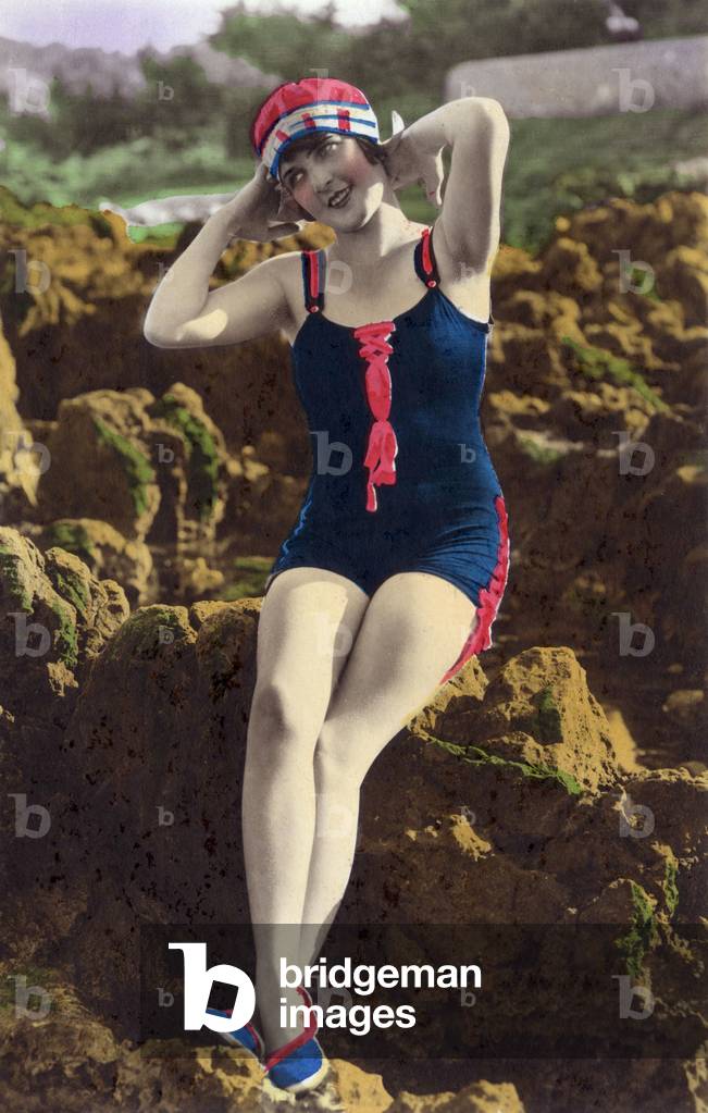 A bather with a bathing suit seated on rocks on the beach, postcard, c. 1920