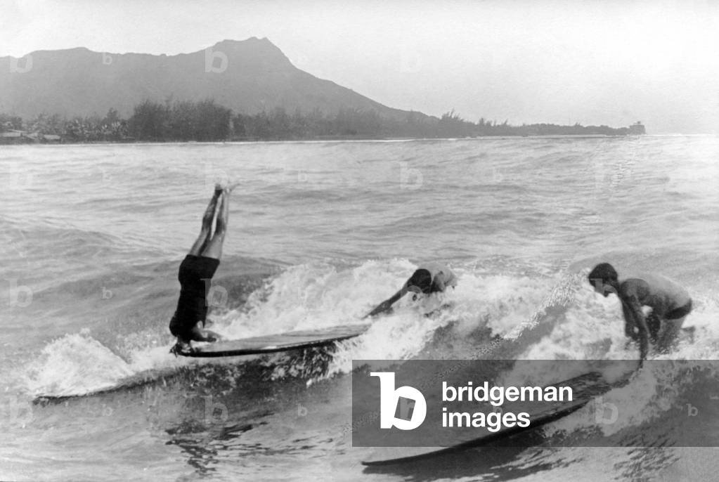 Image of Duke Kahanamoku doing a handstand on a surfboard in