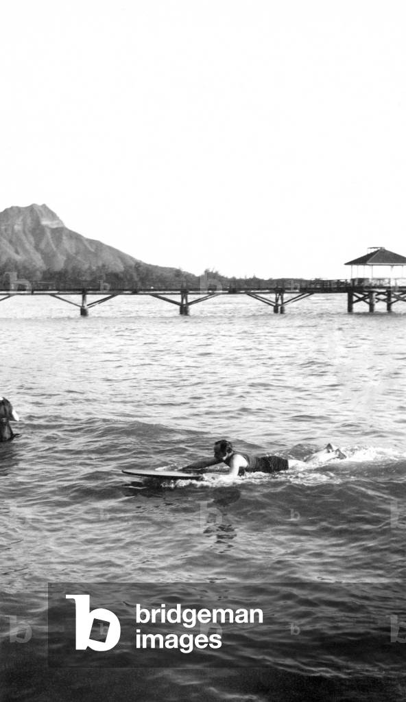 Surfer paddling in off the Moana pier in Waikiki, 1915 (b/w photo)
