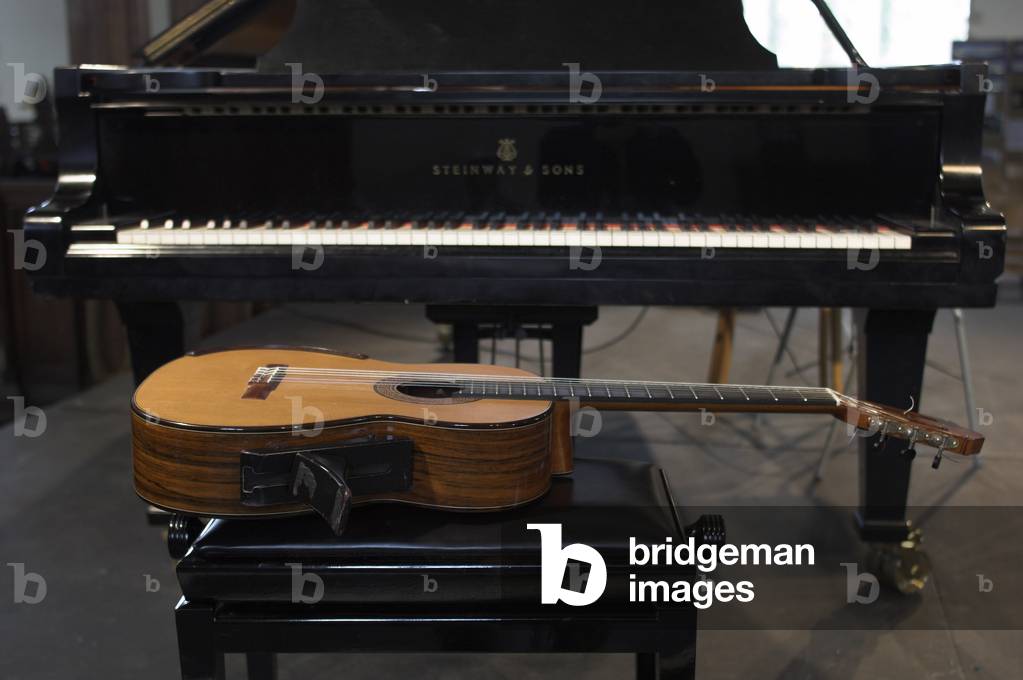Classical guitar lying on a stool in front of a grand piano