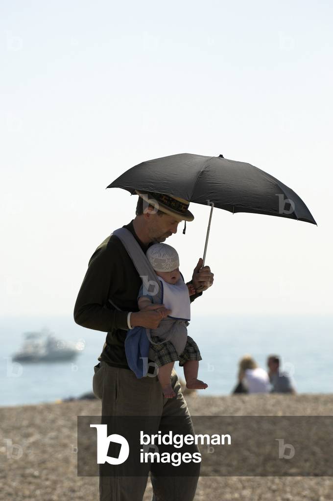 Man with baby and umbrella on Aldeburgh beach, Suffolk, England